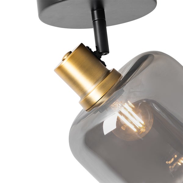 Deckenstrahler mit verstellbarem Gelenk, schwarze Metallbasis, messingfarbene Fassung und Schirm aus Rauchglas.