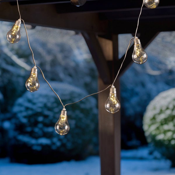 LED Lichterkette für den Außenbereich mit warmweißen Lampen in Glühbirnenoptik vor einer verschneiten Gartenlandschaft.