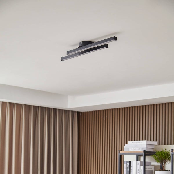 Moderne schwarze LED-Deckenleuchte mit zwei parallelen Lichtbalken an einer weißen Decke in einem hellen Raum mit Holzpaneelen.