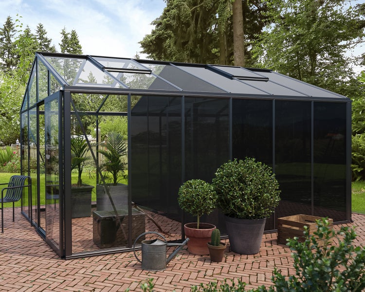 Modernes Gewächshaus mit dunklem Aluminiumrahmen und Glaswänden auf einer gepflasterten Terrasse im Garten.