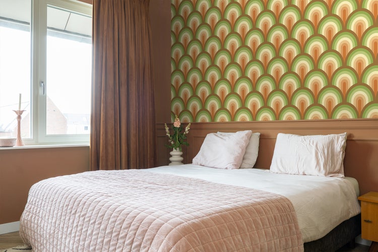 Schlafzimmer mit gemusterten Tapeten, Bett, Kissen und Vorhängen