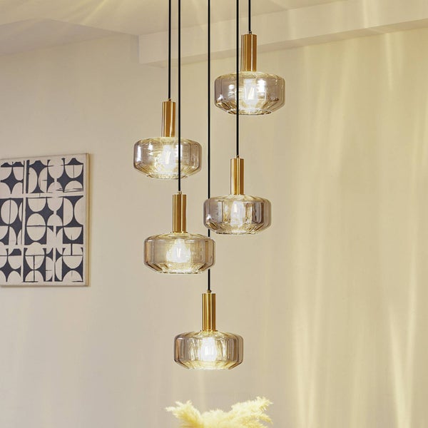 Moderne helle Raumszene mit einer fünfflammigen Pendelleuchte aus Glas und goldfarbenem Metall vor einem geometrischen Wandbild.