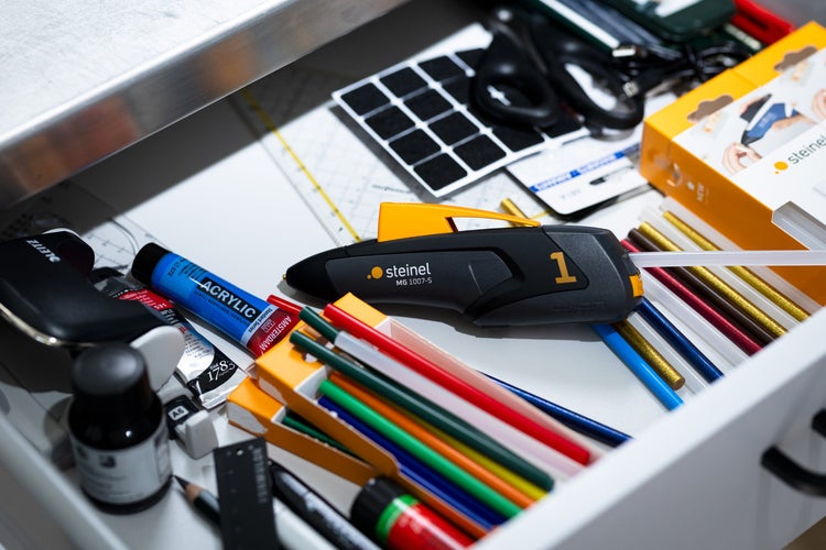 Offene Schublade mit Heißklebepistole, Klebesticks, Acrylfarben und Büromaterial