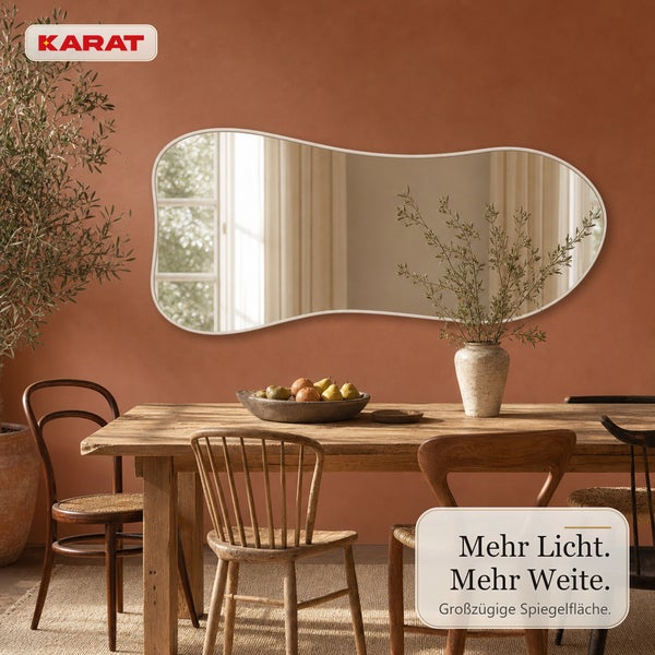 Wandspiegel mit unregelmäßiger, organischer Form und Rahmen über einem Holzesstisch in einem Wohnraum mit Karat Logo.