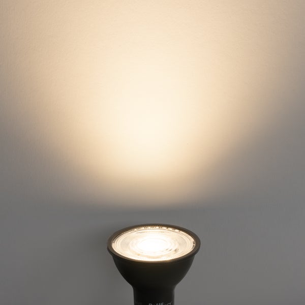 Eingeschaltetes LED-Leuchtmittel in Schwarz mit warmweißem Lichtkegel an einer Wand.