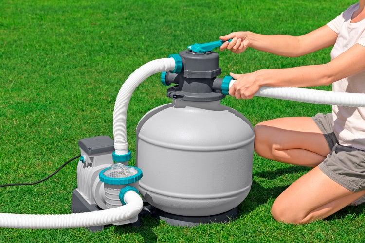 Frau bedient Sandfilteranlage für Schwimmbecken auf Rasen