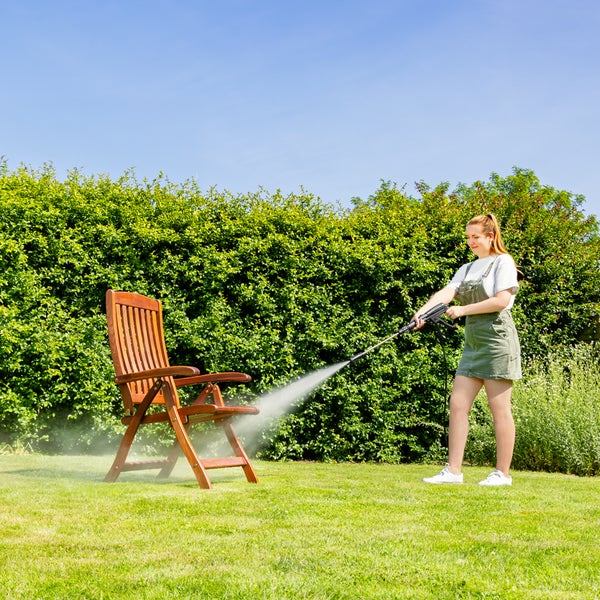 Frau reinigt Holzstuhl mit Hochdruckreiniger im Garten