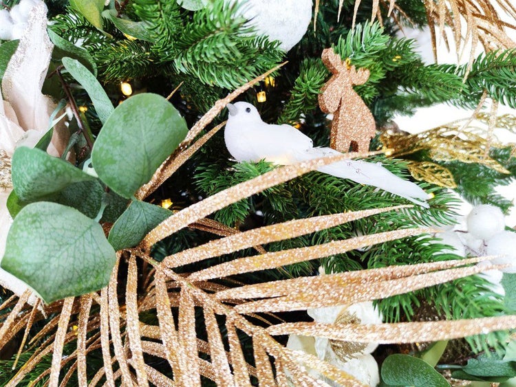 Weihnachtsbaumdekoration mit künstlichen Tannenzweigen, glitzernden Palmenblättern, einer Vogel-Figur und einem Rentier-Anhänger.