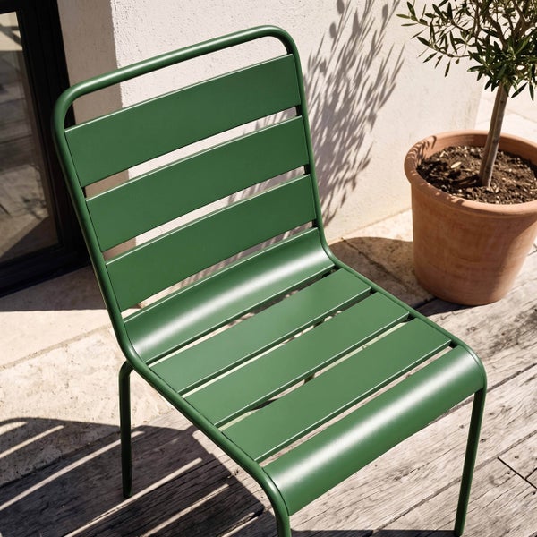 Moderner Gartenstuhl aus grünem Metall mit Lattenstruktur auf einer Holzterrasse neben einem Terrakottatopf mit Pflanze.