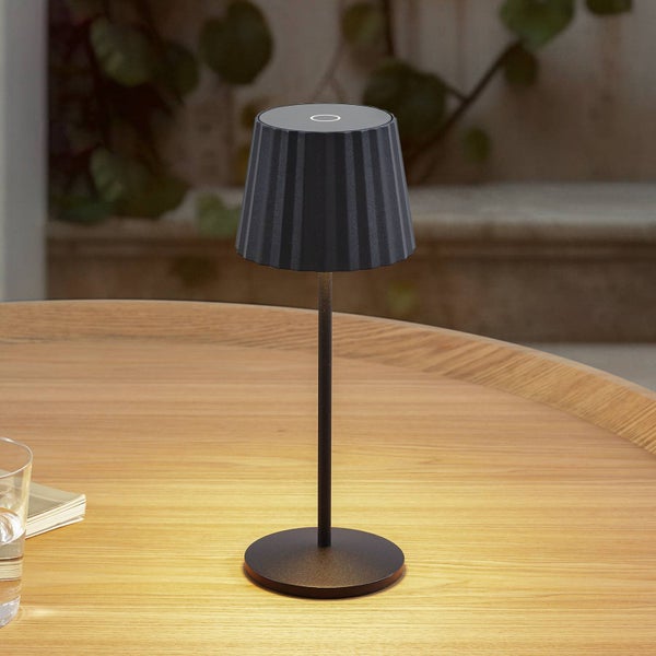 Schwarze LED-Tischleuchte mit plissiertem Schirm auf einem Holztisch im Außenbereich.