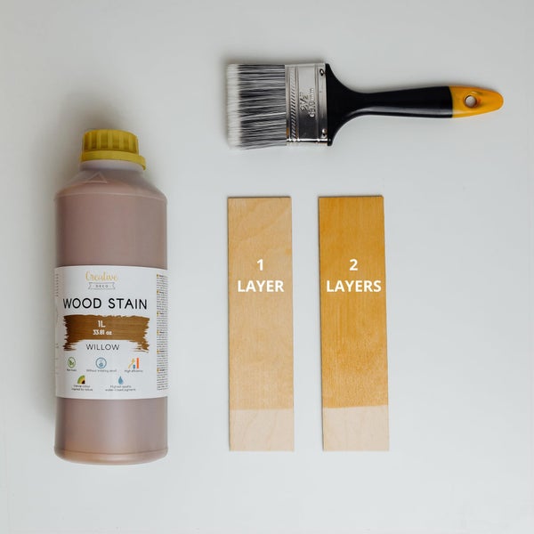 Flasche Creative Deco Holzbeize Willow 1 Liter mit Flachpinsel sowie Farbmuster von einer und zwei Schichten auf Holz.