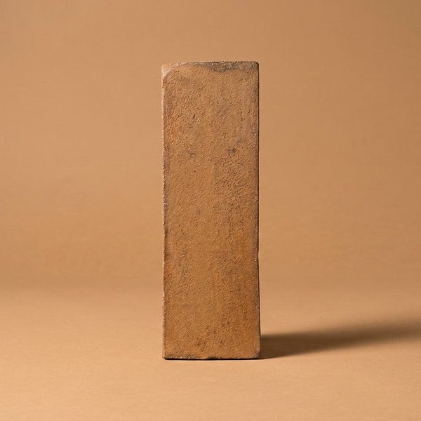 Ein einzelner, rechteckiger Mauerziegel aus Ton in aufrechter Position.