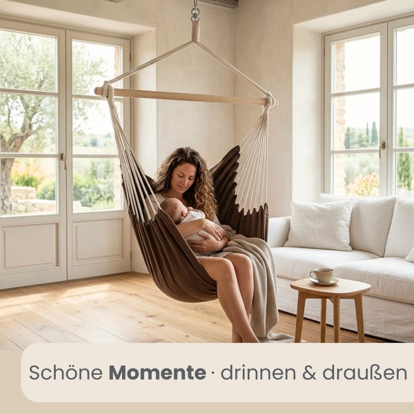 Frau mit Baby in einem Hängesessel aus Stoff in einem hellen Wohnzimmer mit Holzfußboden und Sofa.