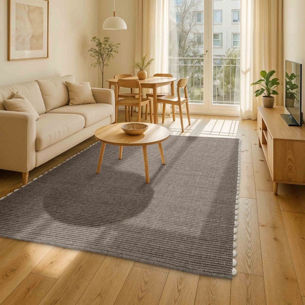 Modernes Wohnzimmer mit gewebtem Teppich auf hellem Holzboden, beigem Sofa, rundem Couchtisch und viel natürlichem Licht.