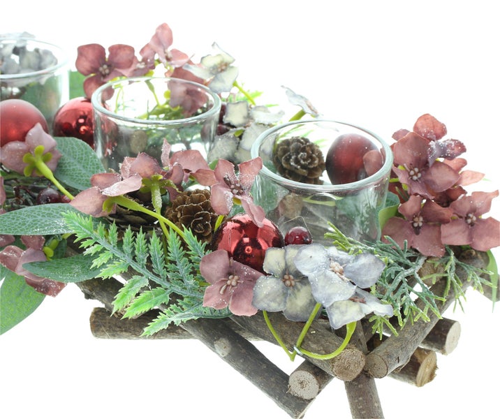Weihnachtliche Tischdekoration mit drei Glaswindlichtern, verziert mit künstlichen Blüten, Tannenzapfen und Weihnachtskugeln auf einem Holzgestell.