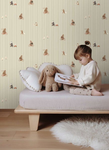 Kindertapete mit Tiermotiven in einem Kinderzimmer, ein Kind liest ein Buch auf einem niedrigen Holzbett mit einem Stoffhasen.