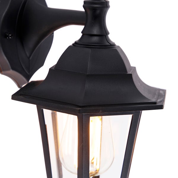 Schwarze Außenwandleuchte in Laternenform aus Metall und Glas mit eingeschaltetem Leuchtmittel.