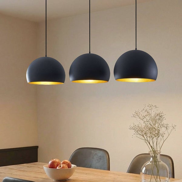 Dreiflammige Pendelleuchte mit halbkugelförmigen Lampenschirmen in Schwarz mit goldener Innenseite über einem Esstisch aus Holz.