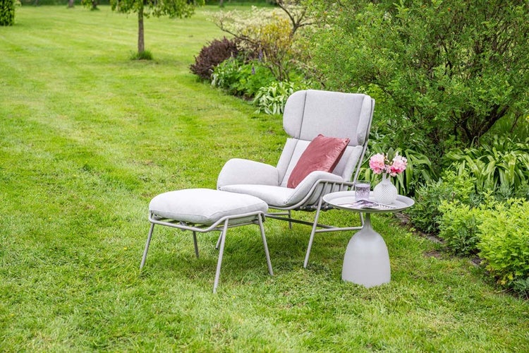 Moderner Garten-Loungesessel mit Hocker und Beistelltisch in einem hellen, gepflegten Garten, hellgraue Polsterung, Metallgestell.