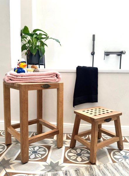 Badezimmer mit zwei Holzschemeln, Handtüchern und Dekorationen auf gemustertem Fliesenboden.