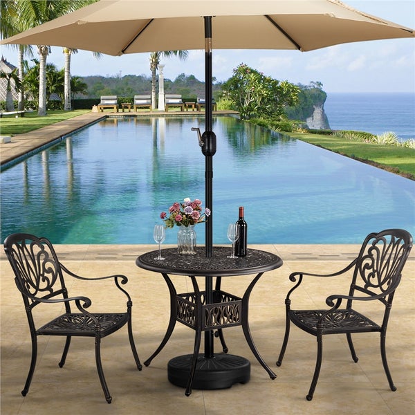 Gartenmöbel-Set aus Metall mit rundem Tisch, zwei Stühlen und großem beigem Sonnenschirm auf einer Terrasse an einem Pool.