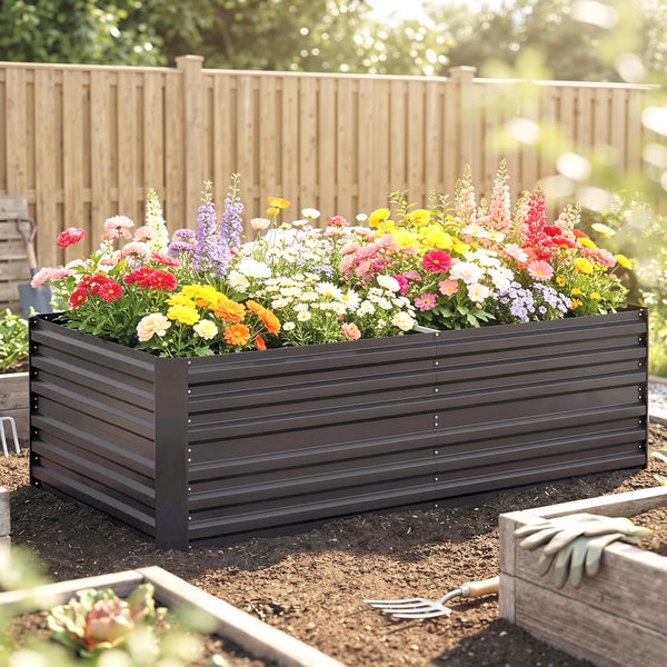 Rechteckiges Hochbeet aus Metall in Anthrazit mit Wellprofil, bepflanzt mit bunten Blumen vor einem Holzzaun im Garten.