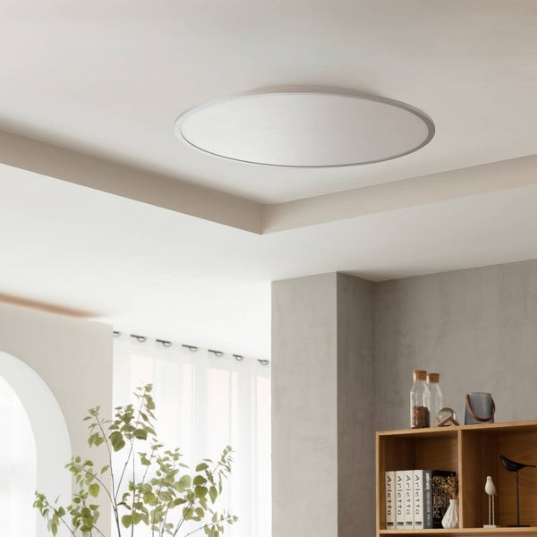 Runde, flache LED Deckenleuchte montiert in einem hellen, modernen Raum mit Holzregal und Zimmerpflanze.