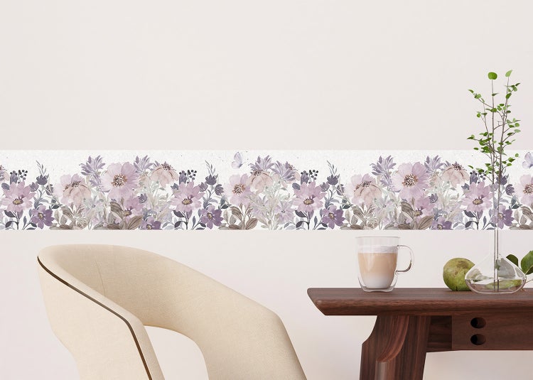 Selbstklebende Tapetenbordüre mit floralem Muster in einem hellen Zimmer über einem Holztisch und einem modernen Sessel.