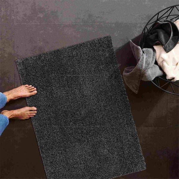 Grauer Badteppich auf Fliesenboden mit Fuß und Handtuchkorb