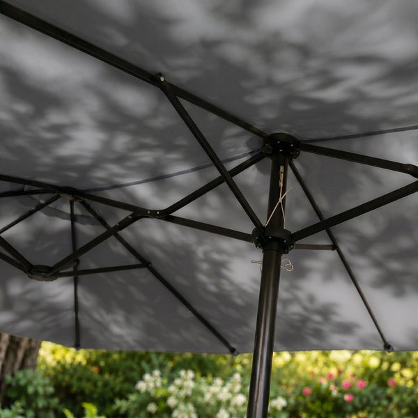 Großer grauer Doppelsonnenschirm über einem runden Gartentisch und zwei Klappstühlen auf einer hellen Terrasse in einem gepflegten, grünen Garten.