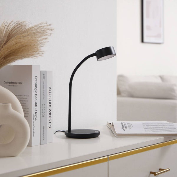 Schwarze LED-Schreibtischlampe mit gebogenem Hals auf einem Sideboard neben Büchern und einer Vase.