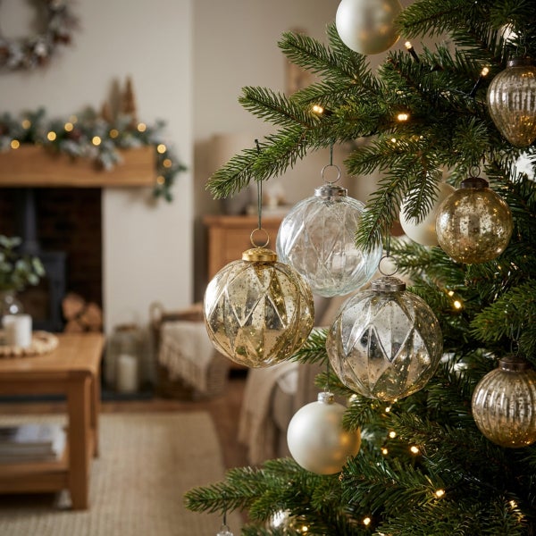 Weihnachtsbaum mit verschiedenen gläsernen Christbaumkugeln in einem gemütlich dekorierten Wohnzimmer.