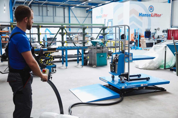 Ein Mitarbeiter bedient einen elektrischen Hubtisch von HanseLifter in einer Industriehalle mit Regalen und Werkzeugmaschinen im Hintergrund.