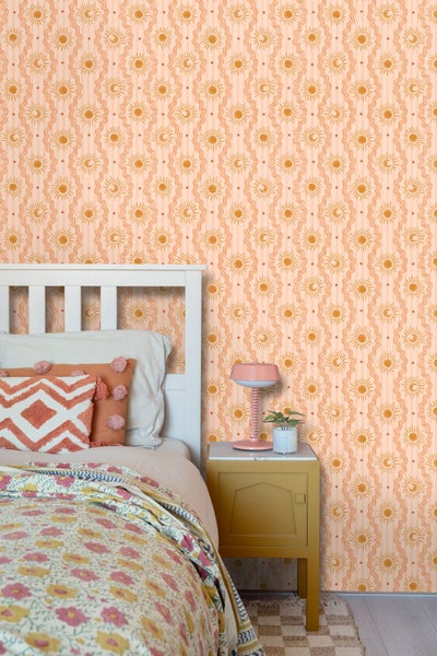 Schlafzimmer mit Tapete mit Sonnen-, Mond- und Sternenmotiven, einem weißen Bett mit gemusterter Bettwäsche und einem gelben Nachttisch.