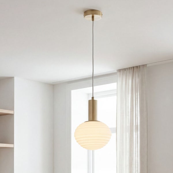 Moderne Pendelleuchte mit gerippter Glaskugel und messingfarbenen Metallelementen in einem hellen Wohnraum.