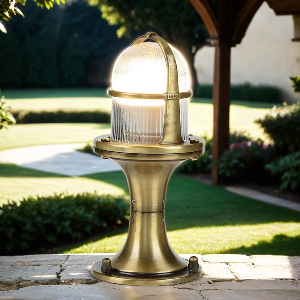 Dekorative Außenleuchte aus Messing auf einer Terrasse mit Garten im Hintergrund.