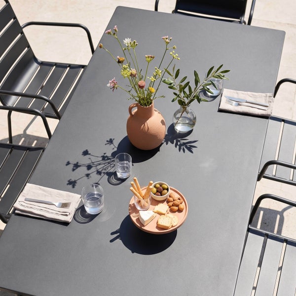Moderner rechteckiger Gartentisch aus Metall mit passenden Stapelstühlen, gedeckt mit Snacks und Blumendeko auf einer sonnigen Terrasse.
