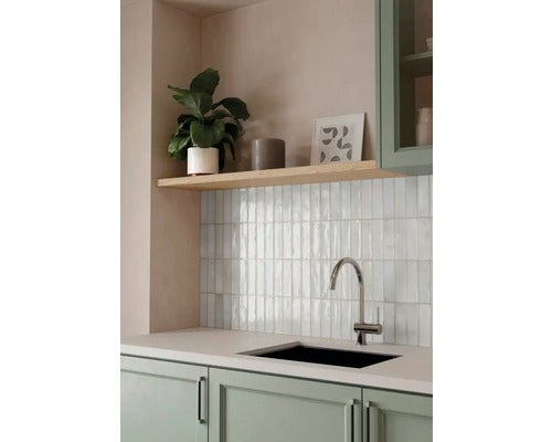 Moderne, helle Küche mit glänzenden Wandfliesen, Arbeitsplatte, schwarzer Spüle, Chrom-Armatur, Holzregal und grünen Schränken.