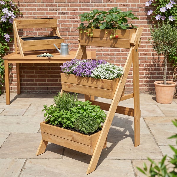 Dreistufige Pflanzentreppe aus Holz auf einer Terrasse mit Erdbeeren, Blumen und Kräutern vor einer Ziegelwand.