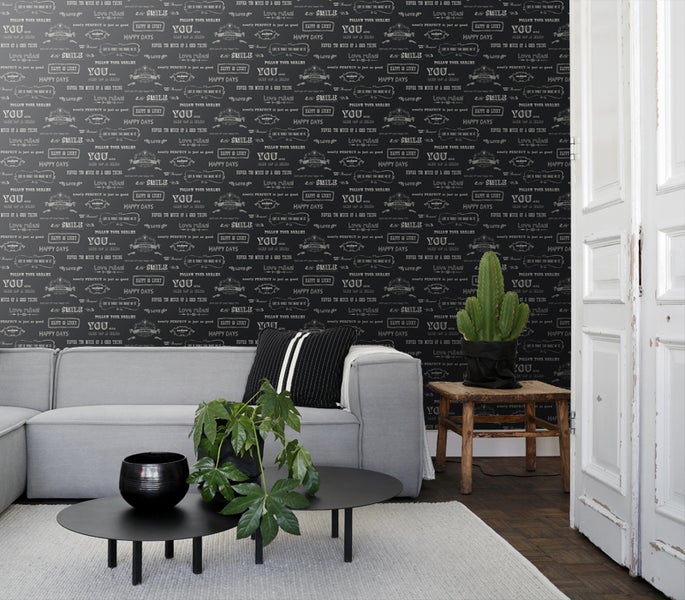 Wohnzimmer mit grauer Couch, Zimmerpflanzen und Tapete mit Schriftzugmuster