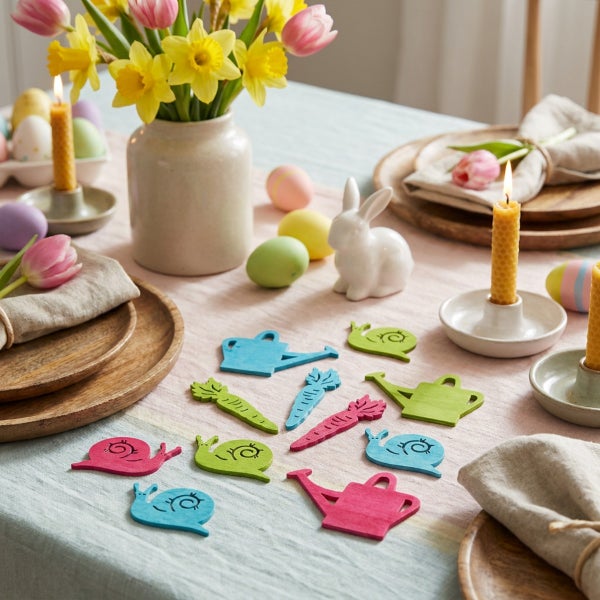 Osterliche Tischdekoration mit bemalten Holzfiguren in Form von Schnecken, Gießkannen und Karotten sowie frischen Frühlingsblumen und Ostereiern.