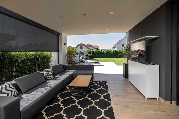 Moderner Außenbereich mit grauer Eckcouch, Couchtisch, Outdoor-Teppich und Fernseher