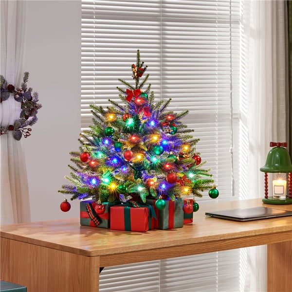 Dekorierter Weihnachtsbaum mit Lichtern und Geschenken auf einem Tisch.