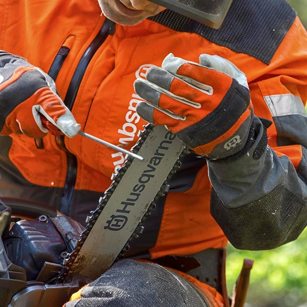 Eine Person schärft eine Husqvarna Kettensäge mit einer Feile.