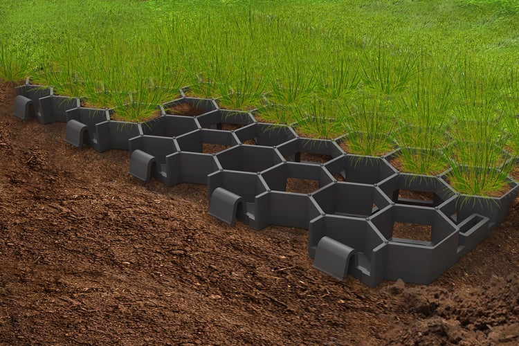 Schwarzes Rasengitter aus Kunststoff in Wabenform, teilweise mit Erde gefüllt und mit Rasen bepflanzt auf Erdboden.