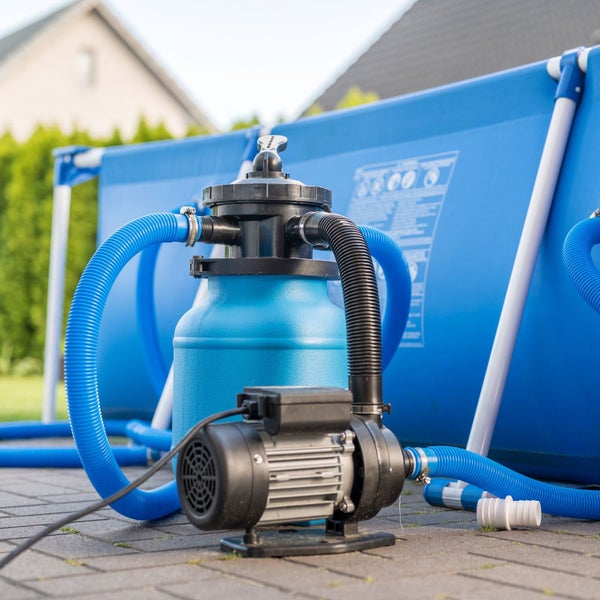 Sandfilteranlage für Swimmingpools mit Pumpe und angeschlossenen Schläuchen vor einem Aufstellpool im Garten.