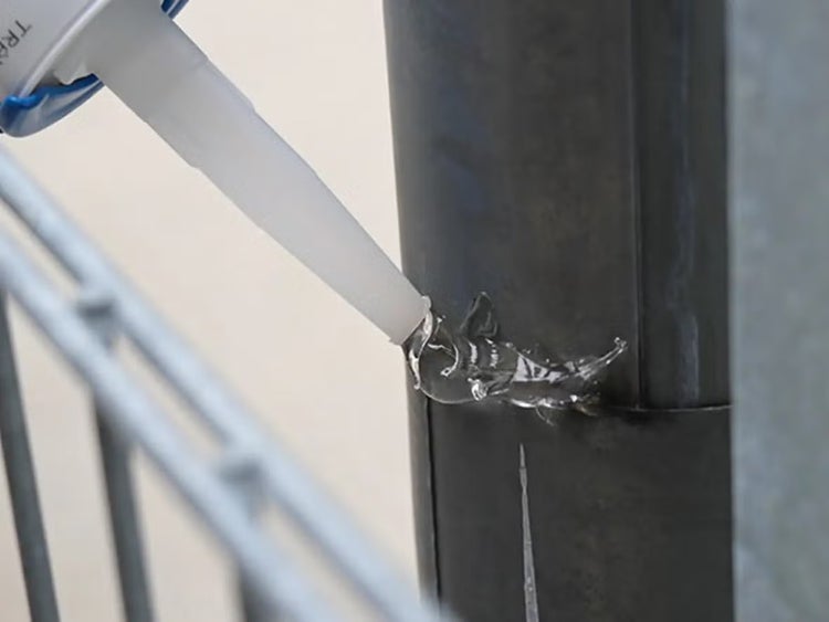 Auftrag von transparentem Dichtstoff mit einer Kartuschenspitze auf ein Metallrohr.