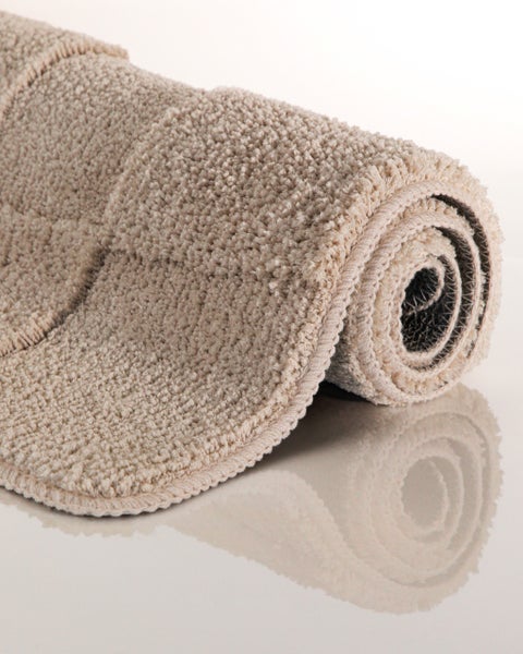 Strukturierte Badematte mit Karomuster auf Boden in Holzoptik neben einer Badewanne.