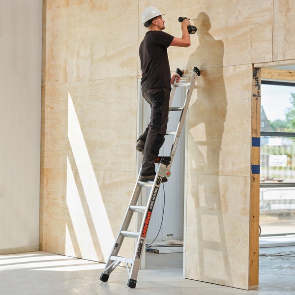 Handwerker auf einer Mehrzweckleiter beim Bohren in eine Wand auf einer Baustelle.