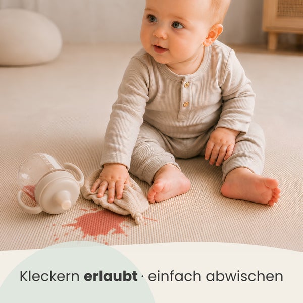 Ein Kleinkind sitzt auf einer leicht zu reinigenden Spielmatte, während es einen verschütteten Fleck mit einem Tuch wegwischt.